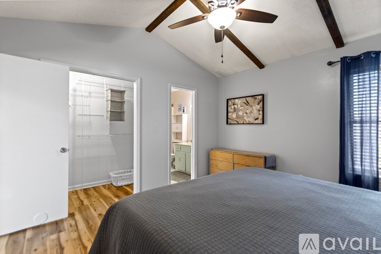 A bedroom with a bed, a ceiling fan, and a door leading to a kitchen.