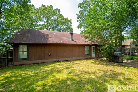 A brown house with a white door and a window is surrounded by trees.