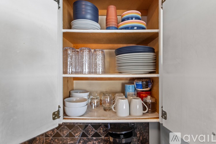 A kitchen cabinet is open, revealing plates, bowls, and glasses.