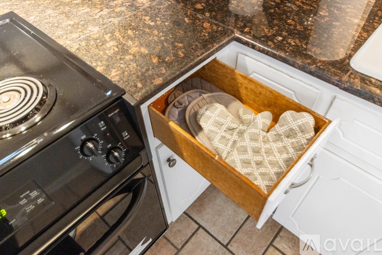 A black oven with a white oven drawer containing a brown oven mitt and a white oven mitt.