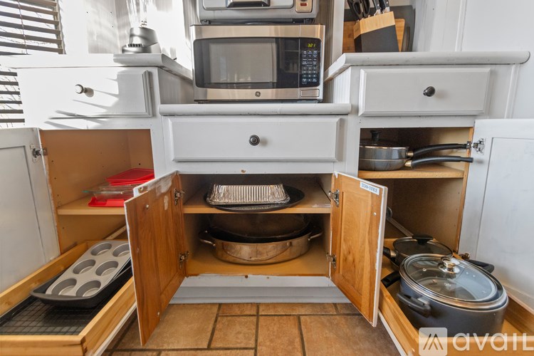 A kitchen with a microwave on top of a cabinet and pots and pans in the cabinet.