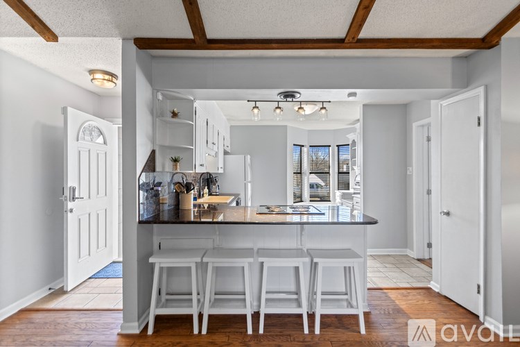 A kitchen with white cabinets and a bar area with white stools.