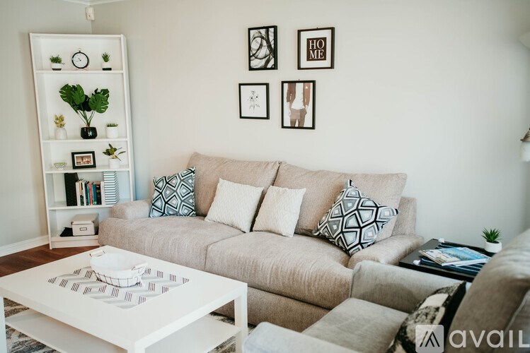 A living room with a beige couch, a white coffee table, and a white shelf with plants and books.