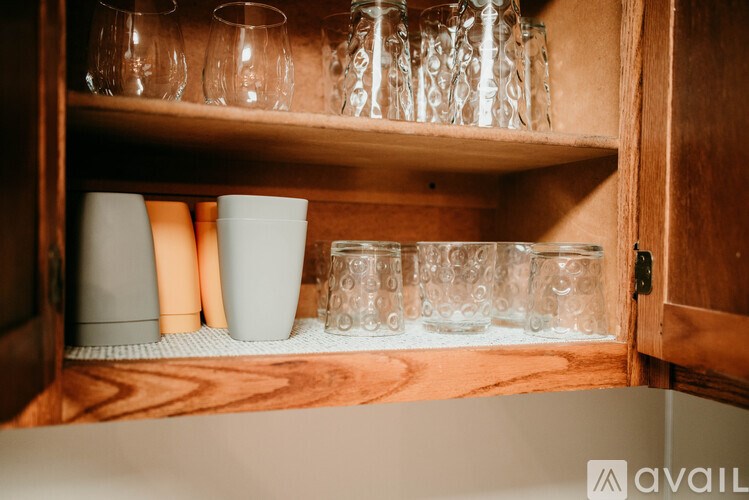 A wooden cabinet with glasses and containers on the shelf.