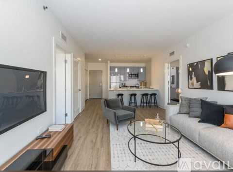 A modern living room with a grey sofa, a glass coffee table, and a television on the left side.