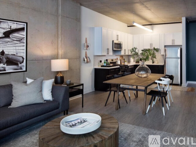 A modern living room with a grey couch, a wooden coffee table, and a kitchen area in the background.