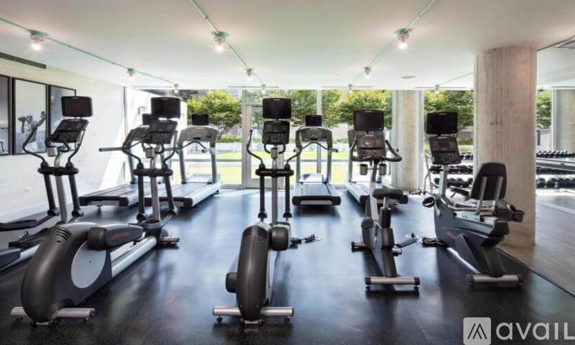A gym with a row of stationary bikes and elliptical machines.
