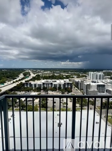 A view from a balcony overlooking a cityscape with buildings and a cloudy sky.
