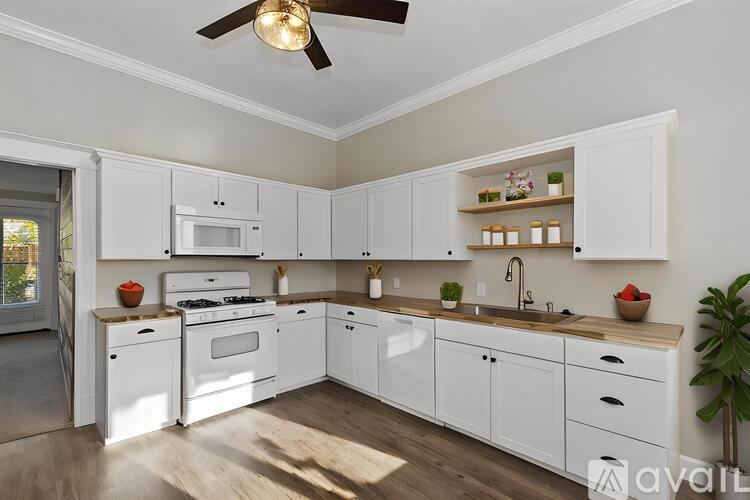 A modern kitchen with white cabinets and appliances, a ceiling fan, and a plant on the counter.