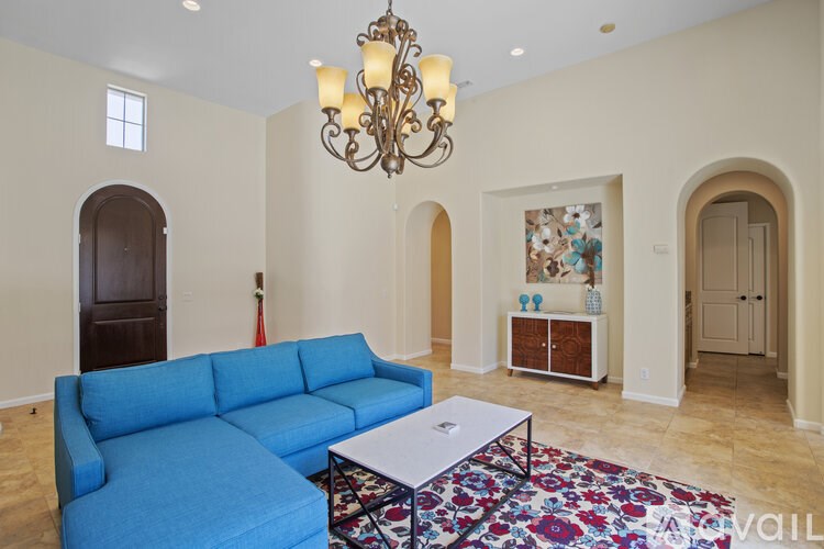 A blue couch sits in a spacious room with a chandelier hanging from the ceiling.