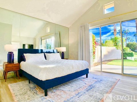 A bedroom with a large bed and a view of the outdoors through the sliding glass doors.