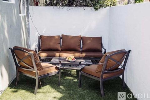 A brown leather sofa and two matching chairs are set on a green lawn.