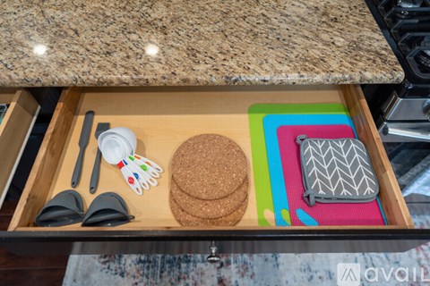 A drawer with a cork coaster, a pair of tongs, a spatula, and a pot holder.