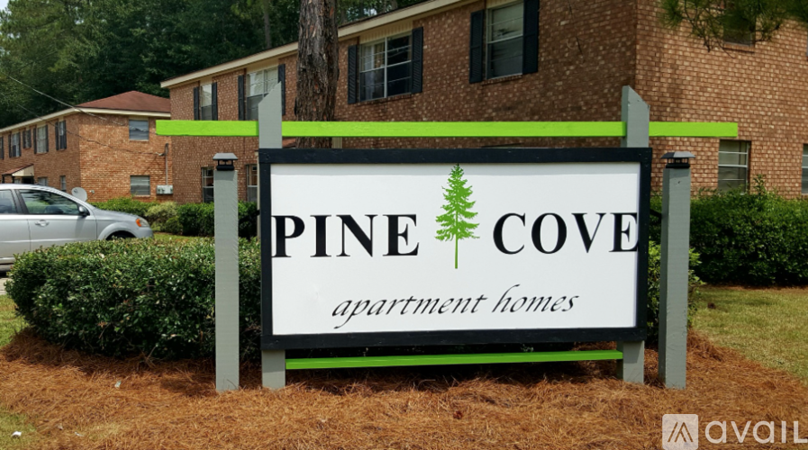 A sign for Pine Cove Apartment Homes is displayed in front of a brick building.