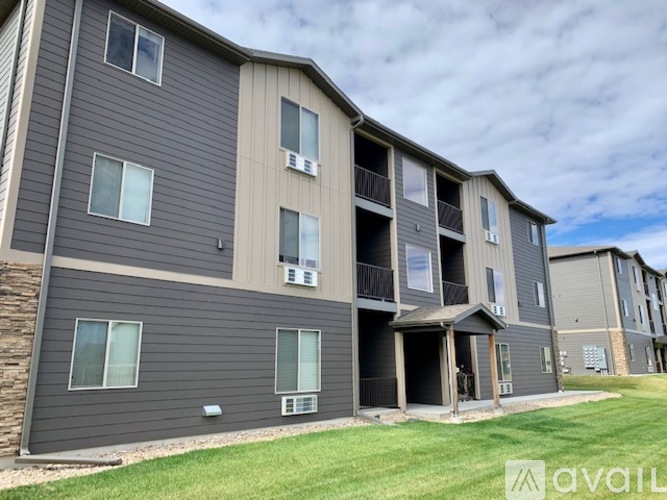A multi-story apartment building with balconies and a grassy area in front.