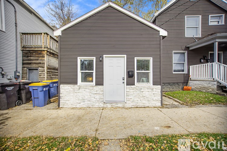 A small house with a white door and windows is in front of a larger house.