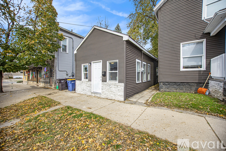 A house with a grey exterior and a white door is surrounded by fallen leaves.