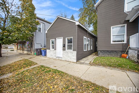 A house with a grey exterior and a white door is surrounded by fallen leaves.