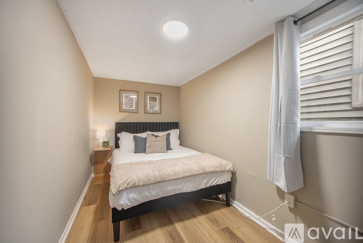 A bedroom with a bed, nightstand, and window with white curtains.
