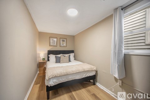 A bedroom with a bed, nightstand, and window with white curtains.