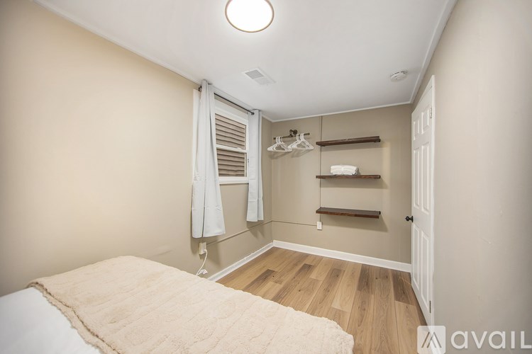A bedroom with a bed, a window with curtains, and a shelf with a coat rack.