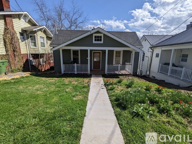 A small house with a front porch is surrounded by a well-kept lawn.
