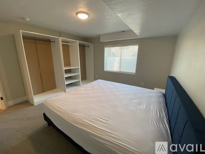 A bedroom with a bed, a window with blinds, and a closet with shelves.