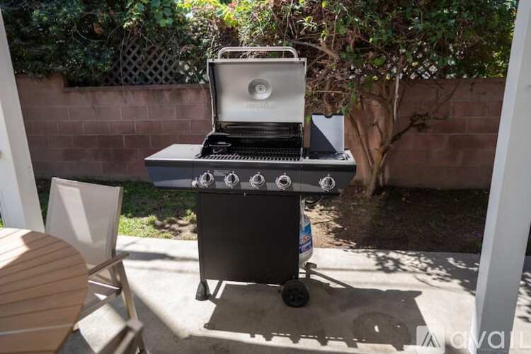 A portable gas grill is on a patio with a chair and table nearby.