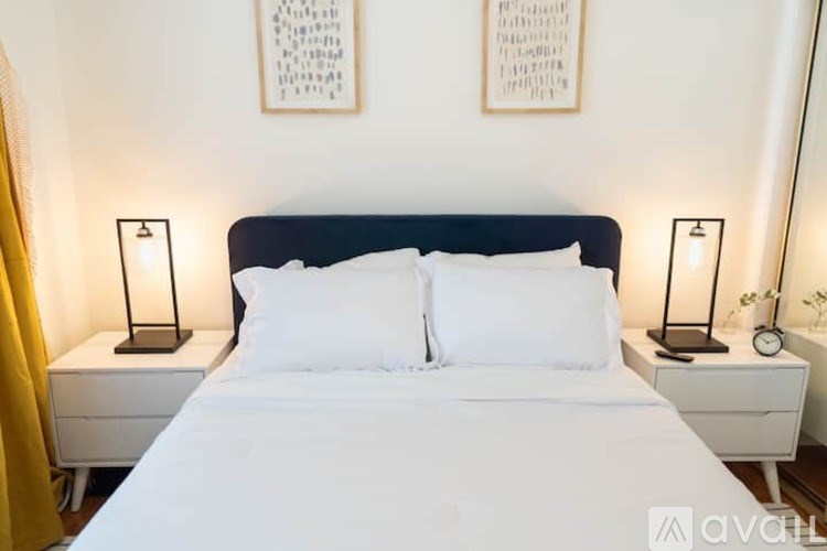 A bed with white pillows and a black headboard is flanked by two black lamps on white nightstands.