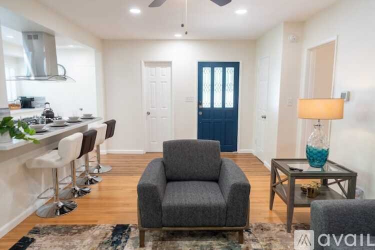 A living room with a grey armchair, a blue door, and a glass table with a lamp on it.