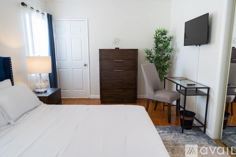 A bedroom with a large bed, a desk with a chair, and a TV mounted on the wall.