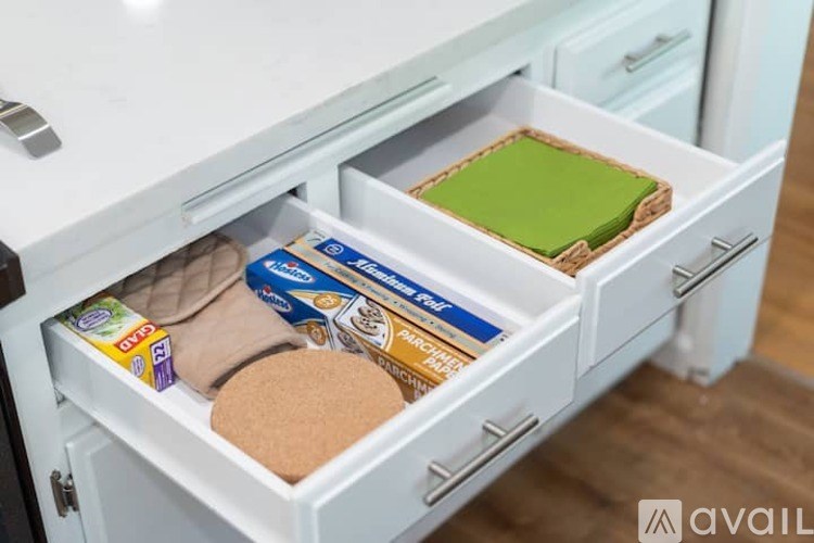 A drawer in a kitchen cabinet contains a green cutting board, a package of bacon, and a package of bread.