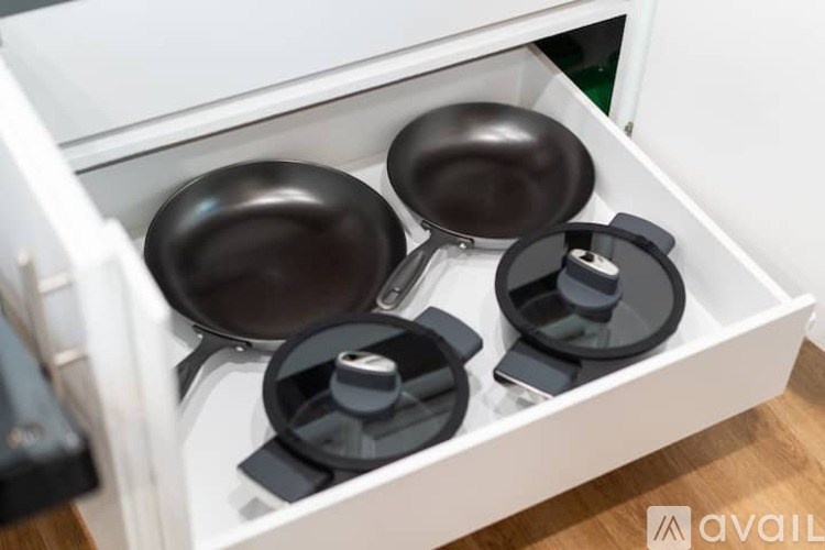 A set of pans and potholders are neatly arranged in a drawer.