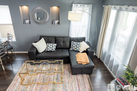 A black couch with a yellow throw pillow sits in front of a grey wall with a mirror and two wall sconces.