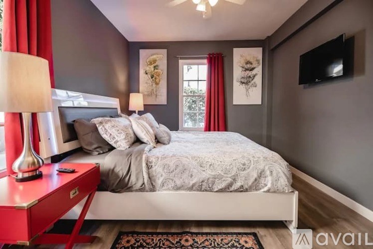 A bedroom with a bed, a red side table, and a television mounted on the wall.