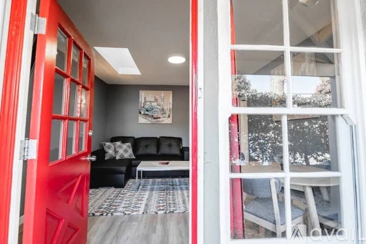 A red door opens to a living room with a black couch and a framed picture on the wall.