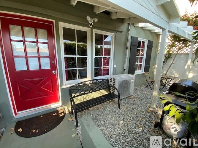 A red door is on the left and a black bench is in the middle of a gravel area.
