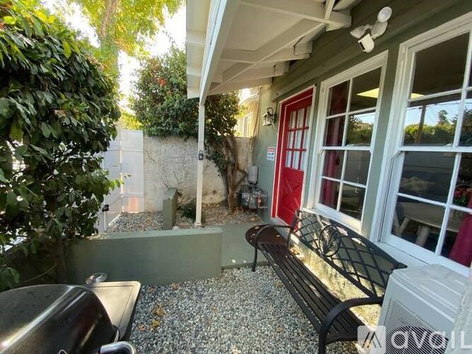 A bench is placed in front of a window with a red door.