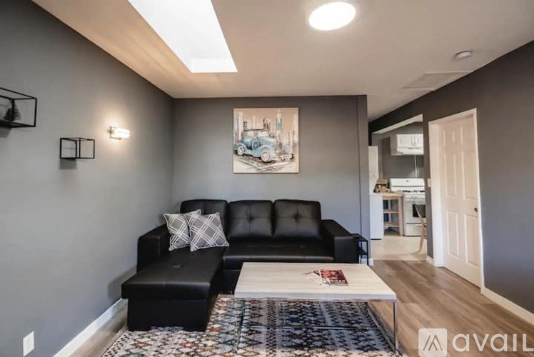 A living room with a black couch and a painting on the wall.