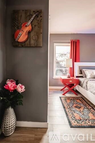 A room with a guitar picture on the wall and a vase with pink flowers.