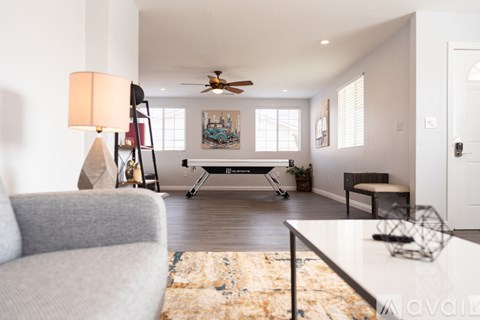 A living room with a grey couch, a rug, a table, a ceiling fan, and a painting on the wall.