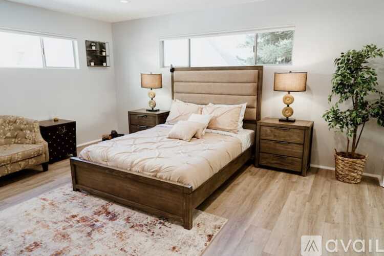 A bedroom with a large bed, two lamps, and a potted plant.