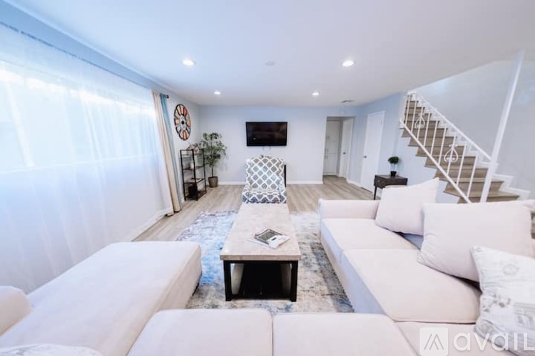 A living room with white furniture and a staircase.
