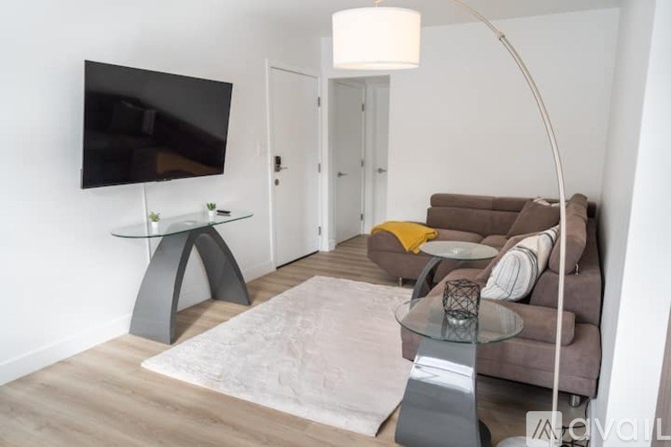 A living room with a grey couch, a white rug, and a black TV mounted on the wall.