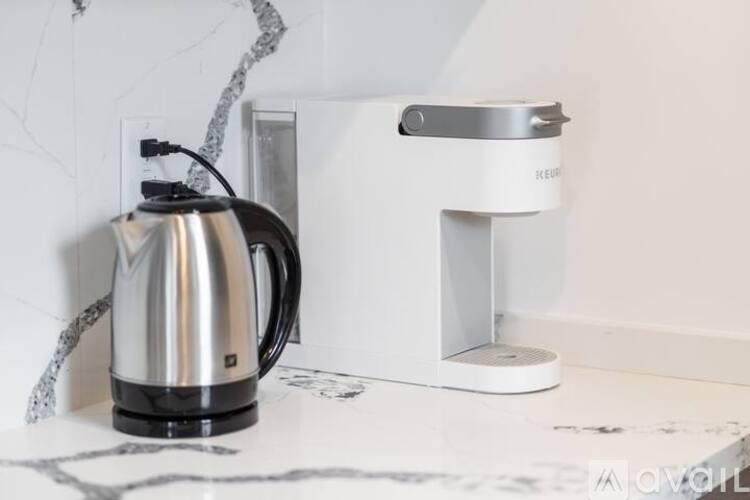 A silver kettle is on a marble countertop next to a white coffee maker.