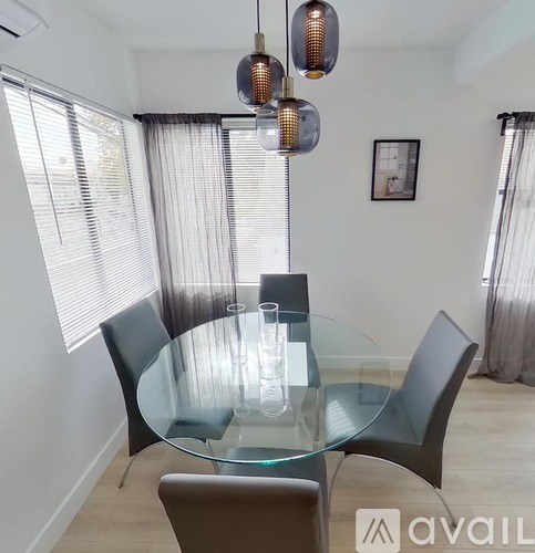 A glass dining table with four chairs and a hanging light fixture.