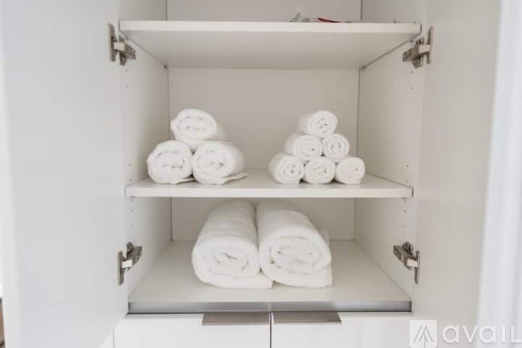 A white cabinet with three shelves, each holding rolled white towels.