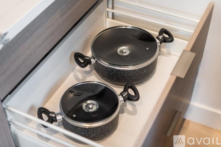 Two black pots with handles are sitting on a white shelf.