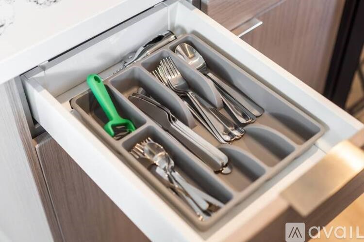A drawer with utensils and a green handle.