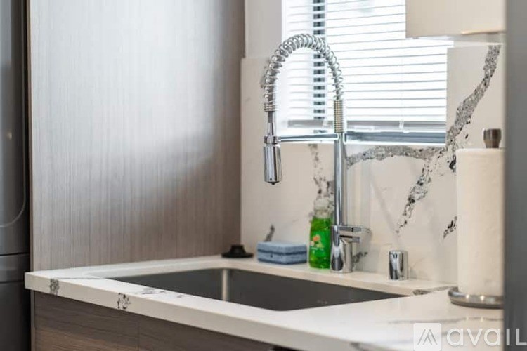 A modern kitchen sink with a chrome faucet and a bottle of soda on the counter.